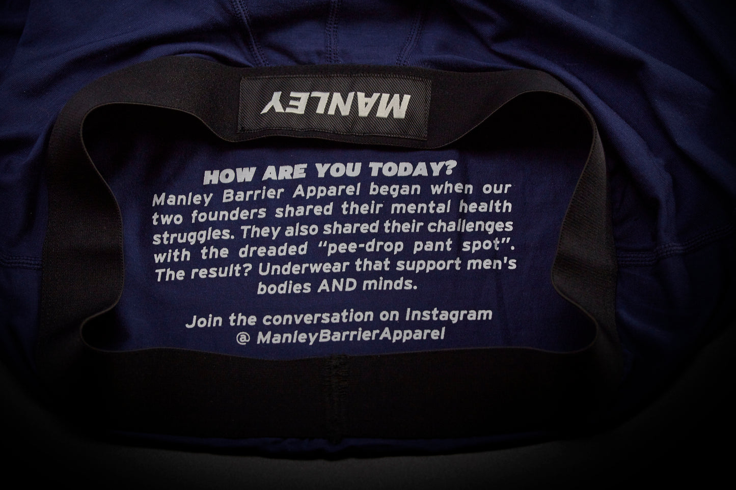 Text on the inside back panel of Manley boxer briefs. Reads: How are you today? Manley Barrier Apparel began when our two founders shared their mental health struggles. They also shared their challenges with the dreaded pee-drop pant spot. The result? Underwear that supports men's bodies and minds. Join the conversation on Instagram @Manley Barrier Apparel.
