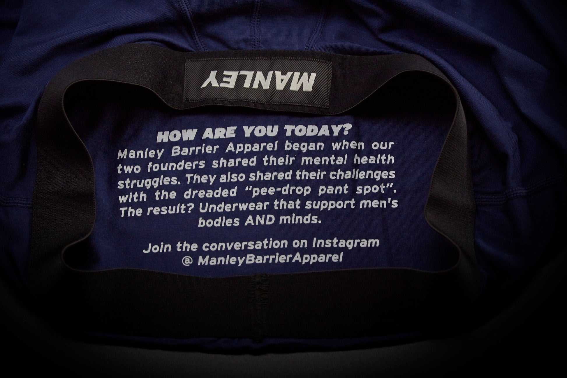 Text on the inside back panel of Manley boxer briefs. Reads: How are you today? Manley Barrier Apparel began when our two founders shared their mental health struggles. They also shared their challenges with the dreaded pee-drop pant spot. The result? Underwear that supports men's bodies and minds. Join the conversation on Instagram @Manley Barrier Apparel. 